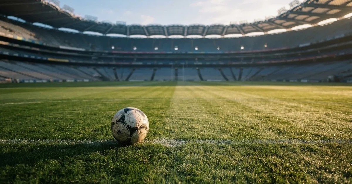 Samotna piłka na murawie ogromnego stadionu o świcie po zakończonej imprezie, trybuny puste.
